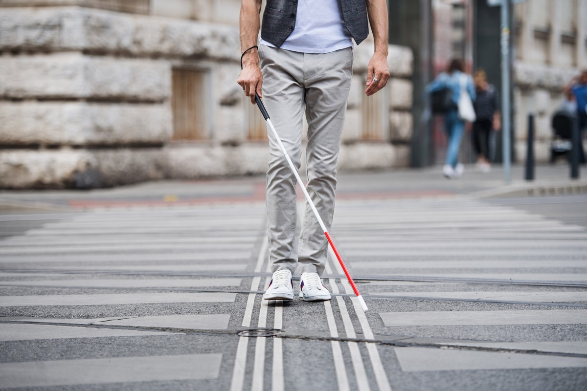 Midsection of young blind man with white cane walking across the street in ...